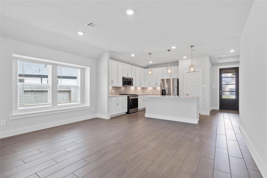 Enjoy meals in this sun-drenched space, featuring durable wood-look tile flooring, abundant natural light from the large windows (fitted with blinds), window seat, sloped ceiling, and recessed lighting.