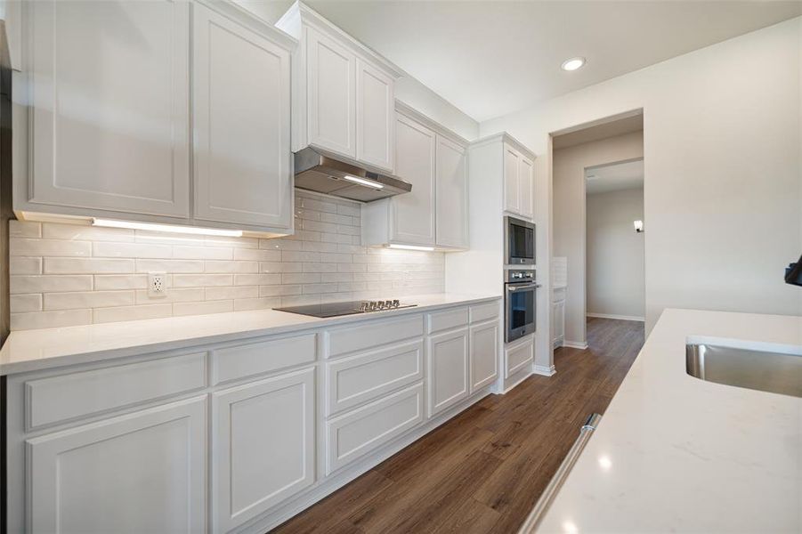 Kitchen featuring white cabinetry, decorative backsplash, light stone countertops, dark wood finished floors, and under cabinet range hood