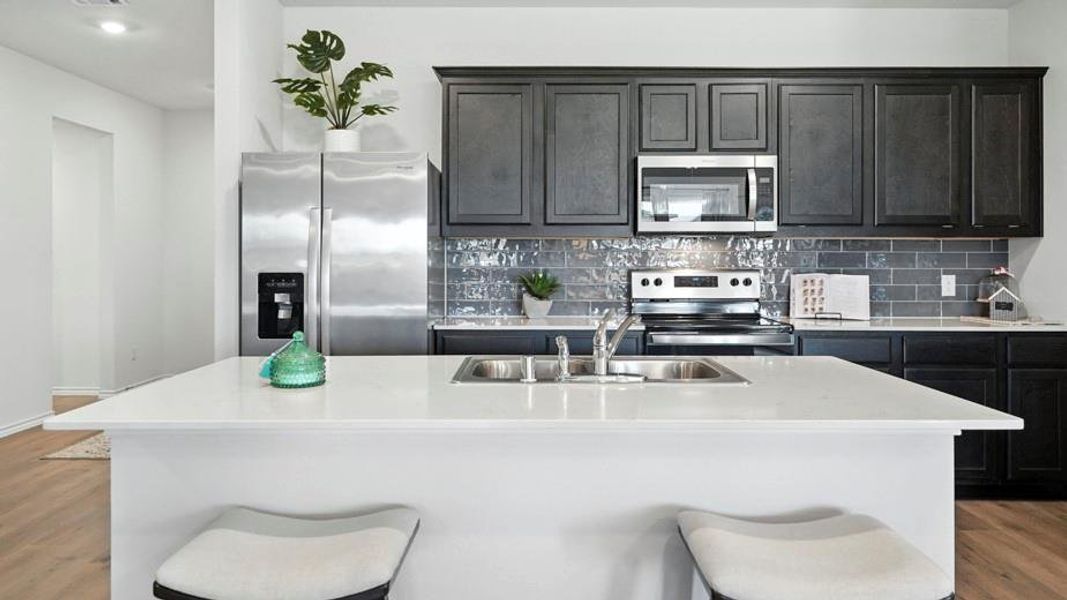 Kitchen featuring light wood-style floors, a kitchen bar, stainless steel appliances, a kitchen island with sink, and light stone countertops Kitchen featuring light wood-style floors, a kitchen bar, stainless steel appliances, a kitchen island with sink, and light stone countertops