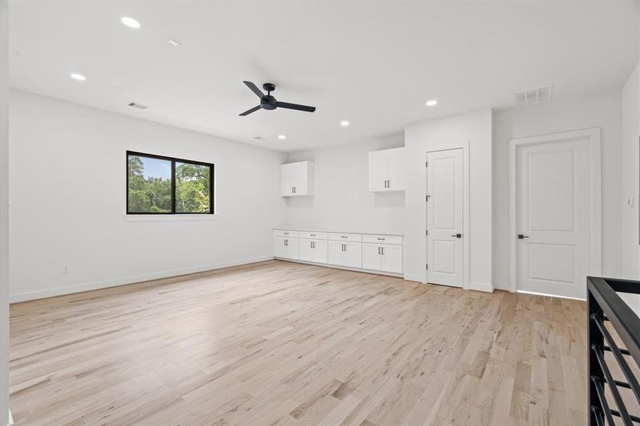 Spacious second-floor game room with wood flooring, recessed lighting, ceiling fan, and elegant white built-ins.