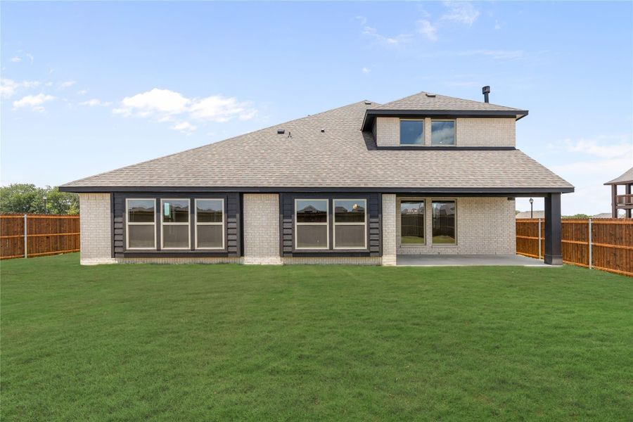 Rear exterior of single-story brick home with large windows, covered patio, and fenced backyard with green lawn. Rear exterior of single-story brick home with large windows, covered patio, and fenced backyard with green lawn.