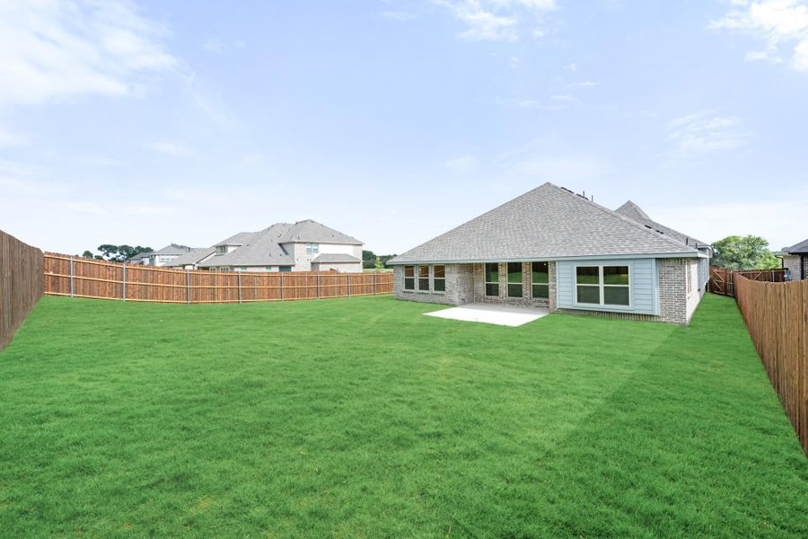 Backyard of brick home with large green lawn, concrete patio, and wood privacy fence