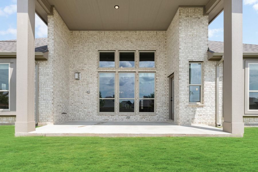 Covered back patio with light brick exterior, large windows, and concrete slab overlooking green lawn Covered back patio with light brick exterior, large windows, and concrete slab overlooking green lawn