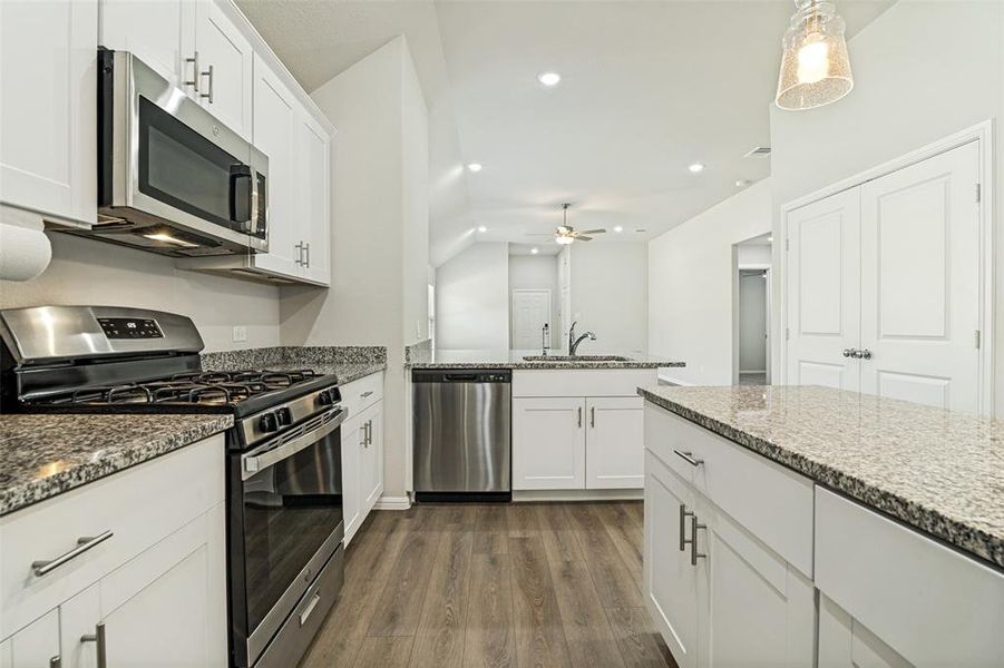 Modern kitchen featuring white cabinetry, stone countertops, stainless steel appliances, wood-finish flooring, and recessed lighting Modern kitchen featuring white cabinetry, stone countertops, stainless steel appliances, wood-finish flooring, and recessed lighting