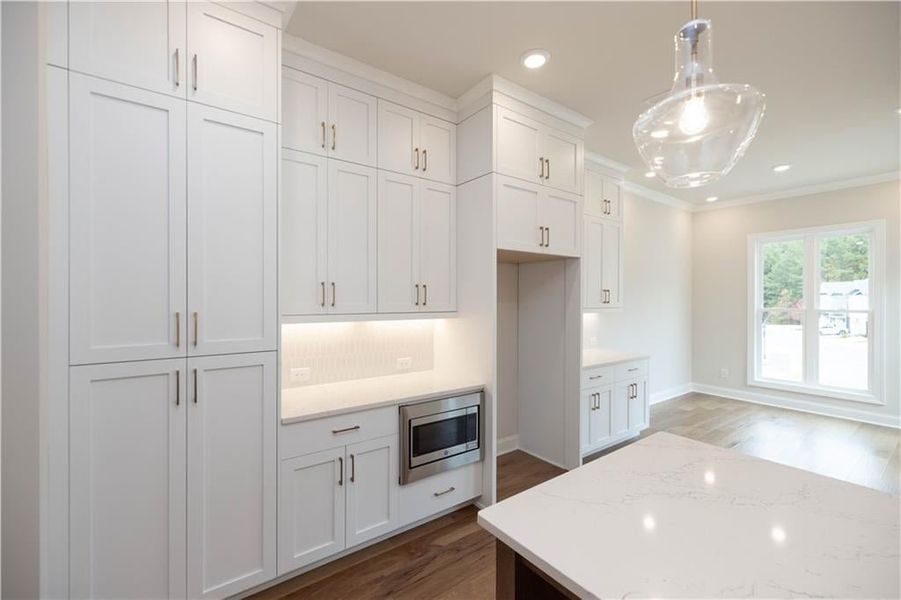 Kitchen featuring stainless steel microwave, hanging light fixtures, white cabinetry, and light stone countertops