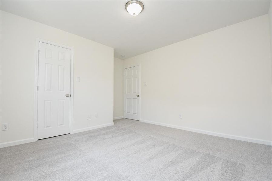 Empty room with beige walls, gray carpet, two closed white doors, and a ceiling light fixture.