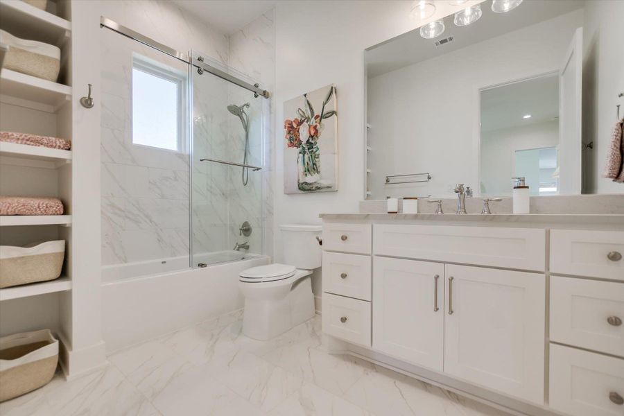 Full bath with marble finish floors, vanity, bath / shower combo with glass door, and toilet Full bath with marble finish floors, vanity, bath / shower combo with glass door, and toilet