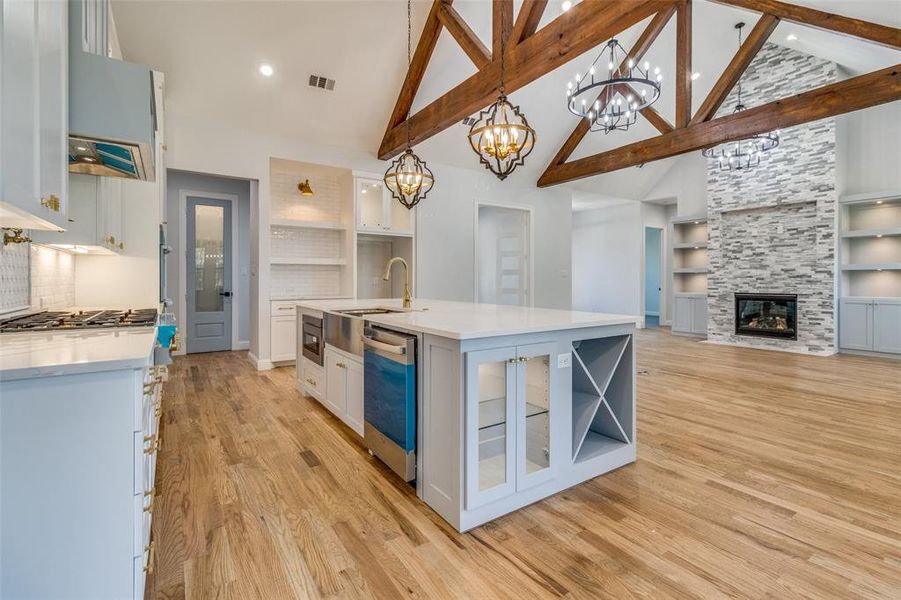 Kitchen featuring white cabinetry, hanging light fixtures, built in features, light hardwood / wood-style floors, and a kitchen island with sink