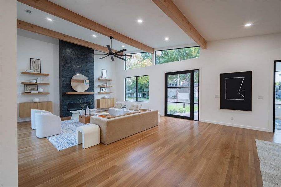 Living room with light wood-type flooring, beamed ceiling, ceiling fan, a fireplace, and a towering ceiling