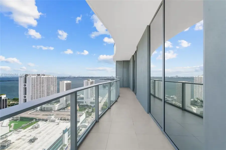 Expansive terrace featuring large-format tile flooring, full-height glass sliding doors, and a sleek glass-paneled railing