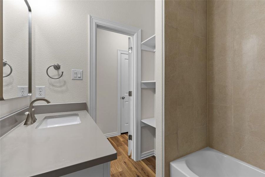 Full bathroom featuring dark wood-style floors, vanity, shower / bath combination, and a textured wall