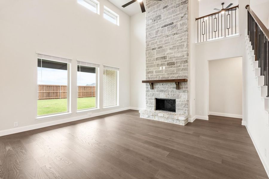Open living room with two-story ceiling, floor-to-ceiling stone fireplace, and dark hardwood floors