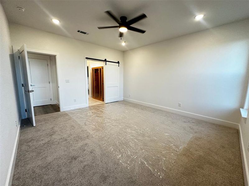 Unfurnished bedroom featuring a barn door, baseboards, visible vents, ensuite bath, and carpet floors