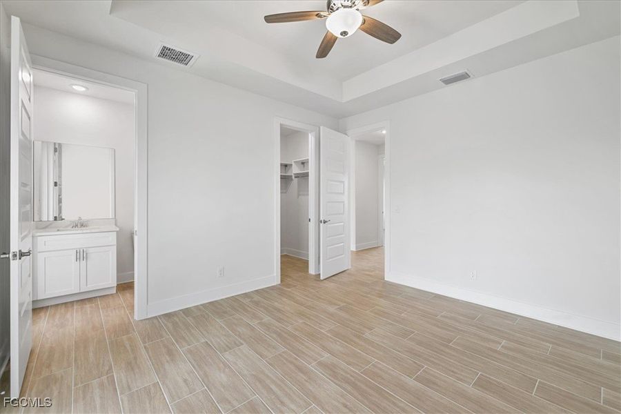 Unfurnished bedroom with a tray ceiling, a walk in closet, ensuite bathroom, and wood finish floors