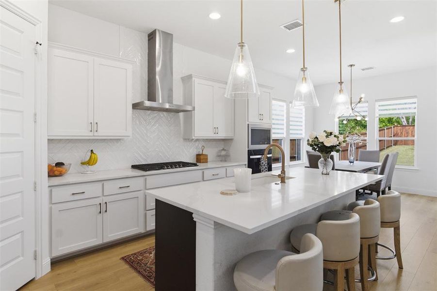 Contemporary kitchen featuring a large central island with a solid surface countertop, white shaker-style cabinetry, stainless steel appliances, and wood-finish flooring