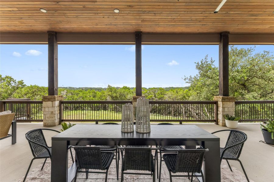 An inviting covered patio offers ample space for outdoor dining, overlooking verdant hills.