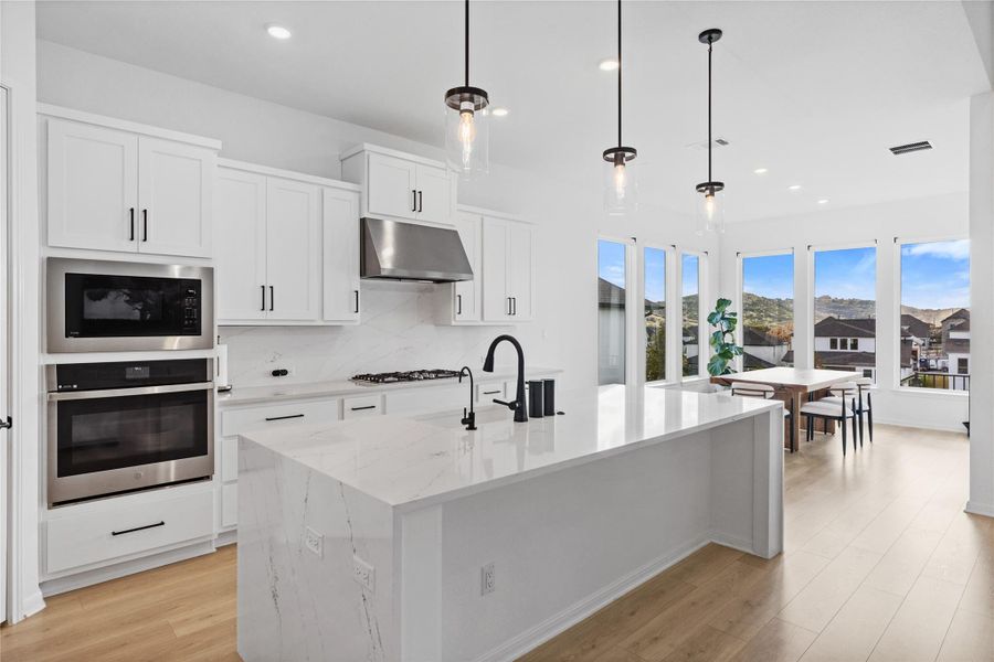 Kitchen with stainless steel appliances, tasteful backsplash, white cabinetry, light wood-style floors, and decorative light fixtures