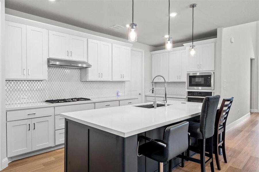 Kitchen featuring sink, light hardwood / wood-style floors, a center island with sink, white cabinets, and appliances with stainless steel finishes