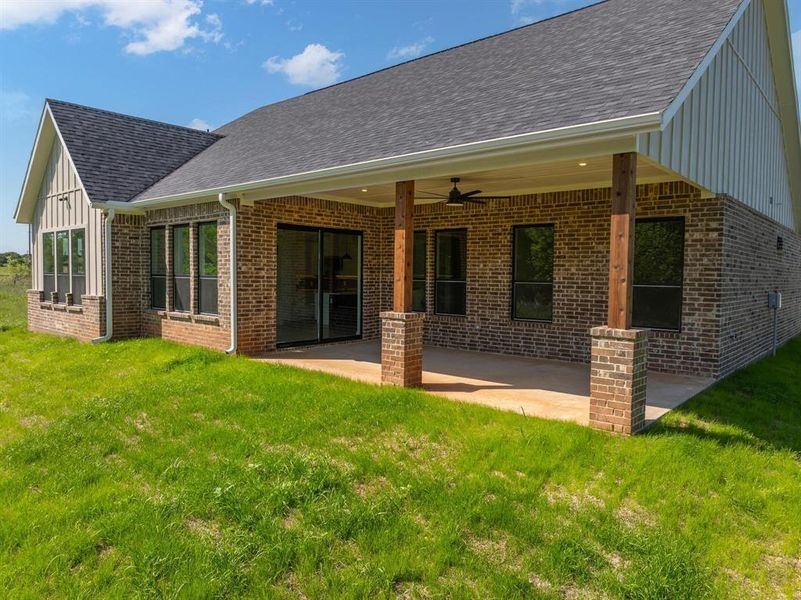 Rear view of house featuring brick siding, a ceiling fan, a patio, and a lawn