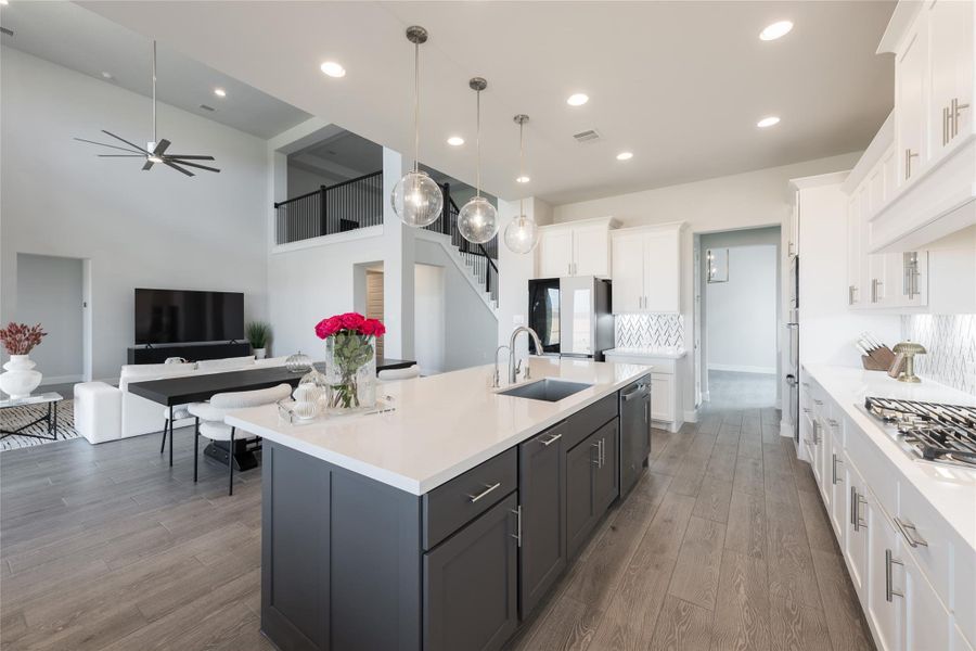 This modern open-concept kitchen and living area features sleek white cabinetry, a large island with a dark finish, and elegant pendant lighting This modern open-concept kitchen and living area features sleek white cabinetry, a large island with a dark finish, and elegant pendant lighting
