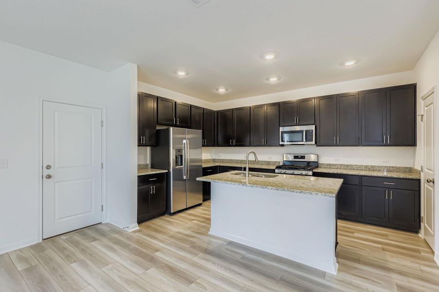 Kitchen with stainless steel appliances, light stone countertops, light wood finished floors, recessed lighting, and an island with sink Kitchen with stainless steel appliances, light stone countertops, light wood finished floors, recessed lighting, and an island with sink