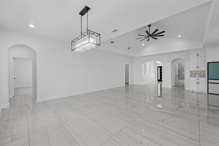 Unfurnished room featuring lofted ceiling, ceiling fan with notable chandelier, and light tile patterned flooring