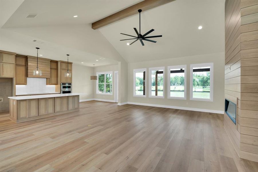 Unfurnished living room featuring high vaulted ceiling, ceiling fan, light hardwood / wood-style floors, a fireplace, and beamed ceiling