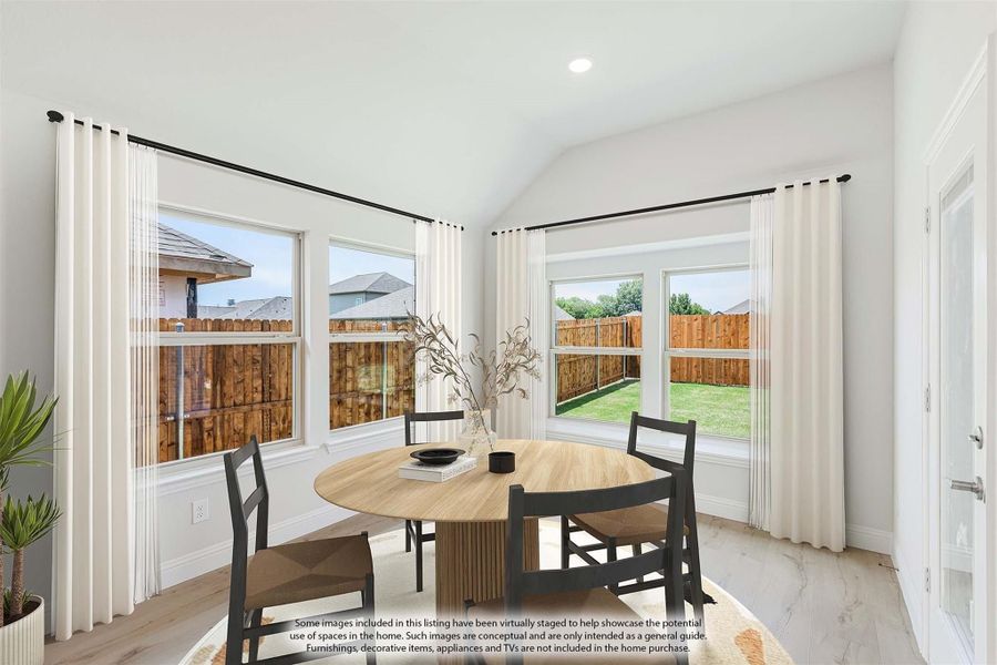 Dining area with round wood table, dark chairs, vaulted ceiling, and large windows overlooking backyard
