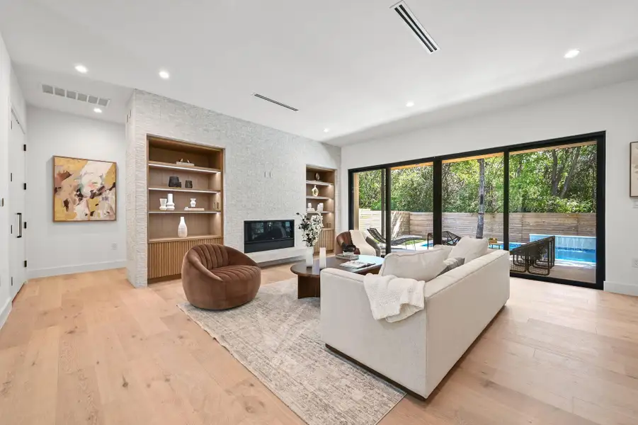 Living room featuring built in features, recessed lighting, a large fireplace, and light wood-style floors