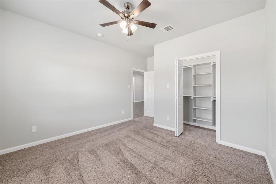 Unfurnished bedroom featuring a closet, ceiling fan, a spacious closet, and carpet flooring