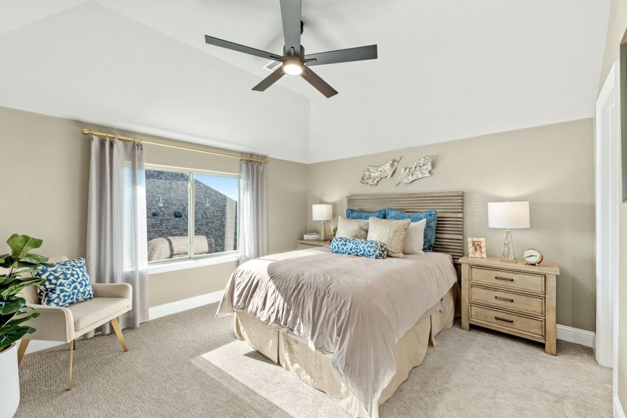 Bedroom with vaulted ceiling, ceiling fan, king bed, wood nightstands, and carpet flooring Bedroom with vaulted ceiling, ceiling fan, king bed, wood nightstands, and carpet flooring