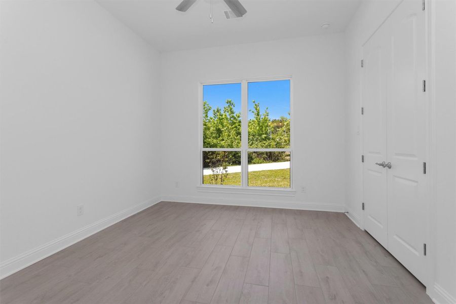 This light-filled secondary bedroom features wood-look tile flooring, a spacious closet, and peaceful views of the lush, tree-lined grounds. This light-filled secondary bedroom features wood-look tile flooring, a spacious closet, and peaceful views of the lush, tree-lined grounds.