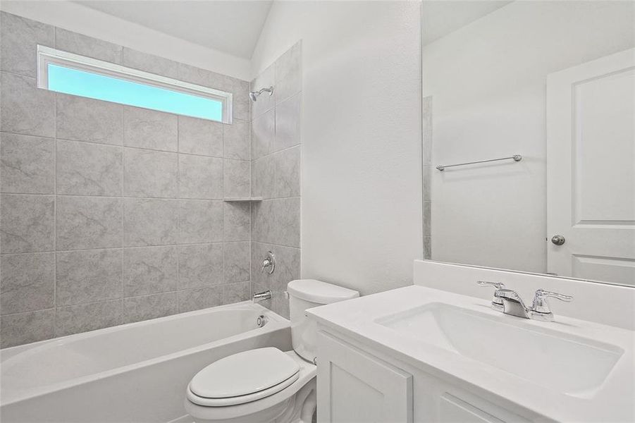 Full bathroom with lofted ceiling, tiled shower / bath combo, vanity, and toilet