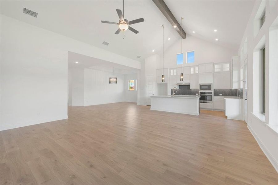 Open-concept living space featuring wood-finish flooring, a vaulted ceiling with exposed beam, and a contemporary kitchen Open-concept living space featuring wood-finish flooring, a vaulted ceiling with exposed beam, and a contemporary kitchen