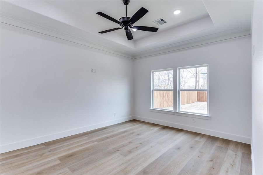 Spare room featuring a tray ceiling, visible vents, light wood-style flooring, a ceiling fan, and baseboards