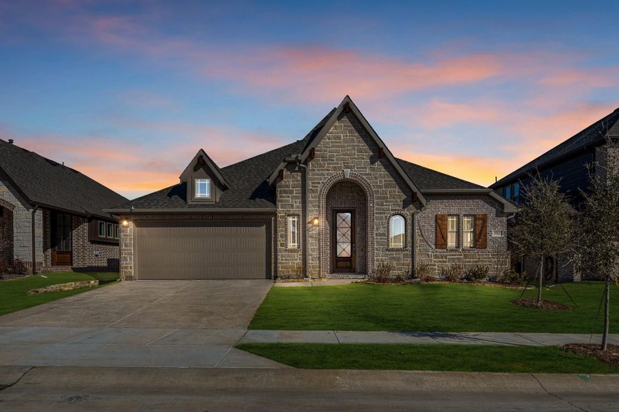 Single-story stone home with arched entry, two-car garage, and green front lawn at dusk Single-story stone home with arched entry, two-car garage, and green front lawn at dusk