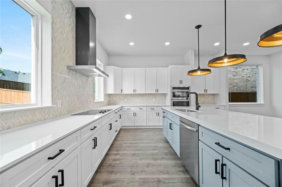 Kitchen featuring appliances with stainless steel finishes, wall chimney range hood, decorative backsplash, white cabinetry, and light countertops Kitchen featuring appliances with stainless steel finishes, wall chimney range hood, decorative backsplash, white cabinetry, and light countertops