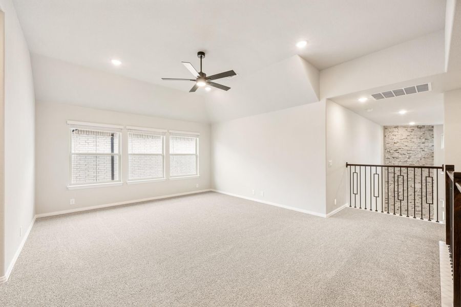Open upstairs bonus room with carpet, ceiling fan, vaulted ceiling, and iron stair railing with stone accent wall nearby.