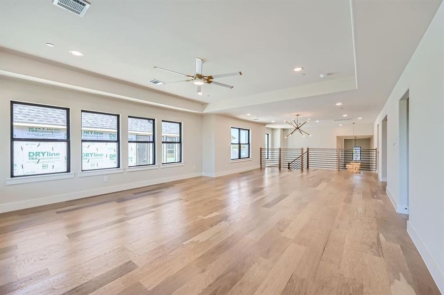 Unfurnished living room with light hardwood / wood-style flooring, ceiling fan, and a tray ceiling