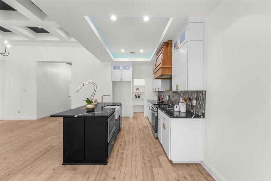 Kitchen with white cabinetry, decorative backsplash, glass insert cabinets, a center island with sink, and light wood-type flooring