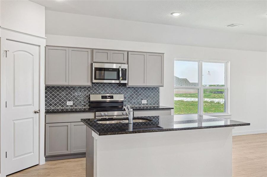 Kitchen featuring stainless steel appliances, gray cabinets, decorative backsplash, light wood-type flooring, and dark stone counters