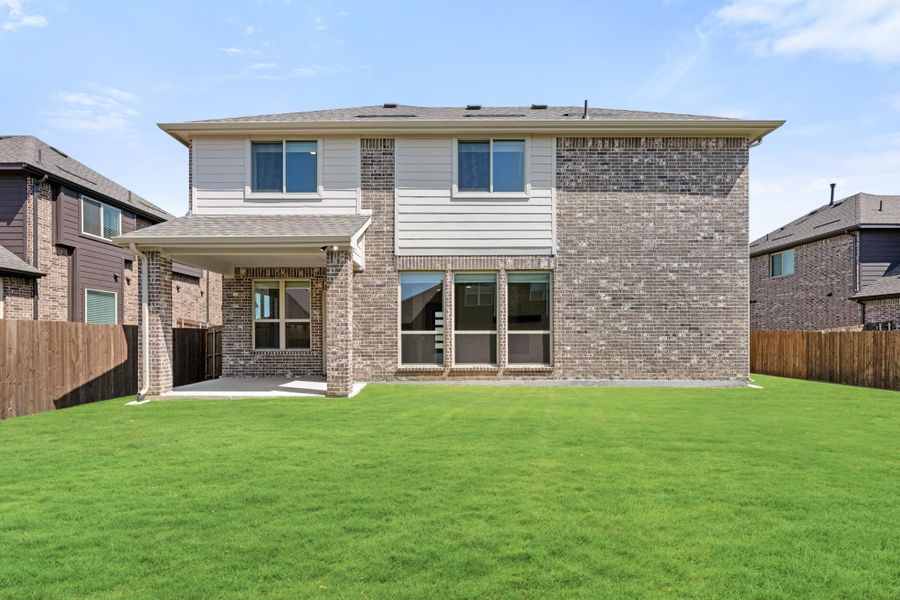 Two-story brick home rear view with covered patio, large backyard, and wood privacy fence