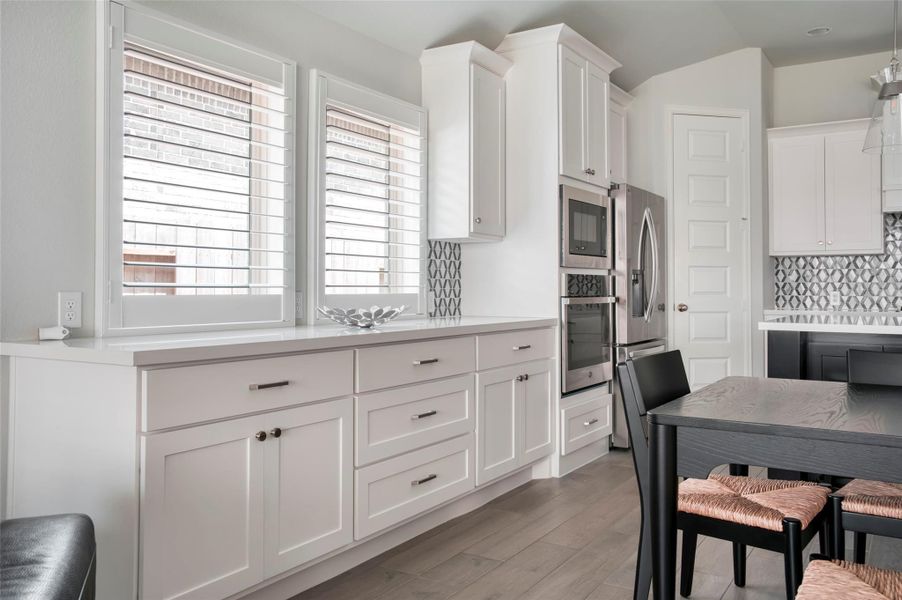 This kitchen features modern white cabinetry, stainless steel appliances, and a stylish backsplash. It includes ample natural light from large windows, and a sleek dining area with hardwood flooring. This kitchen features modern white cabinetry, stainless steel appliances, and a stylish backsplash. It includes ample natural light from large windows, and a sleek dining area with hardwood flooring.