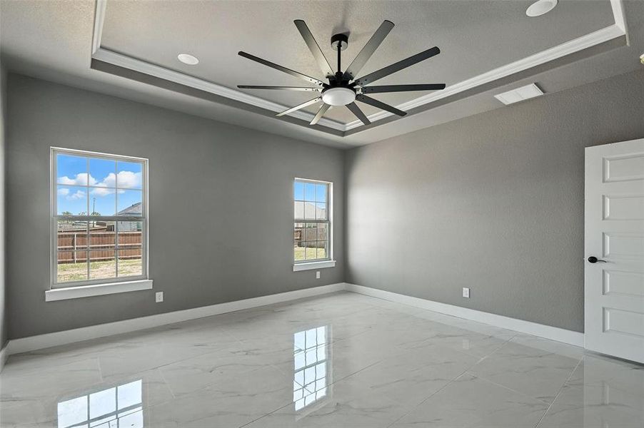 Empty room featuring light marble finish floors, a tray ceiling, and ceiling fan Empty room featuring light marble finish floors, a tray ceiling, and ceiling fan