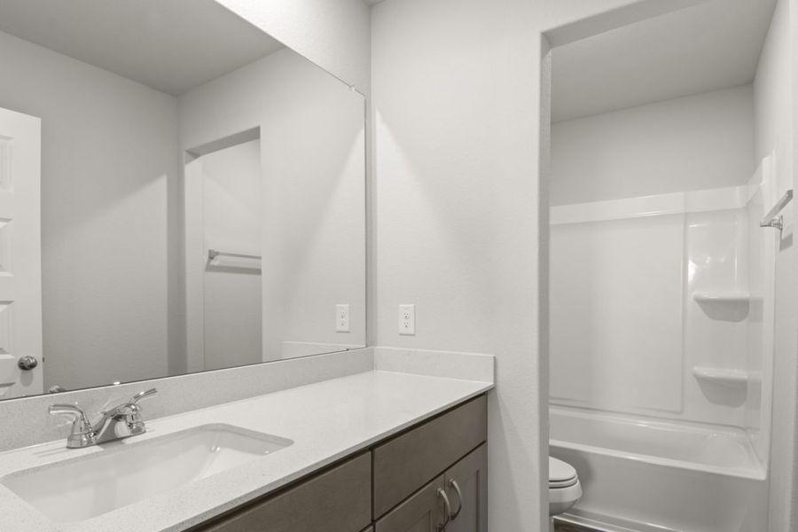 Image of a bathroom with a semi private water closet and white vinyl shower, and a white vanity with a mirror and brown cabinets