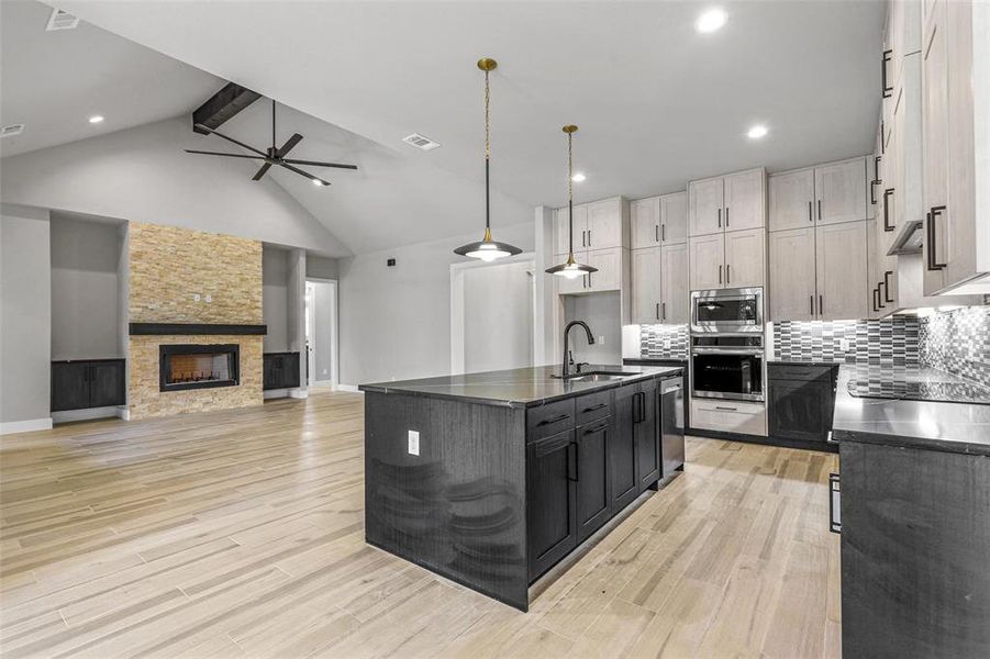 Kitchen with a center island with sink, a stone fireplace, stainless steel appliances, light hardwood / wood-style flooring, and sink