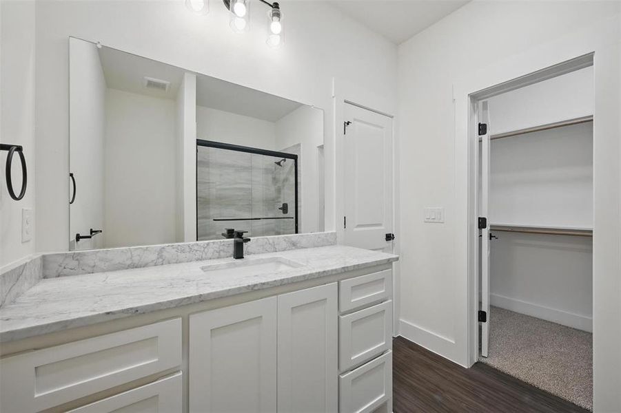 Full bathroom with vanity, baseboards, a stall shower, visible vents, and wood finished floors Full bathroom with vanity, baseboards, a stall shower, visible vents, and wood finished floors