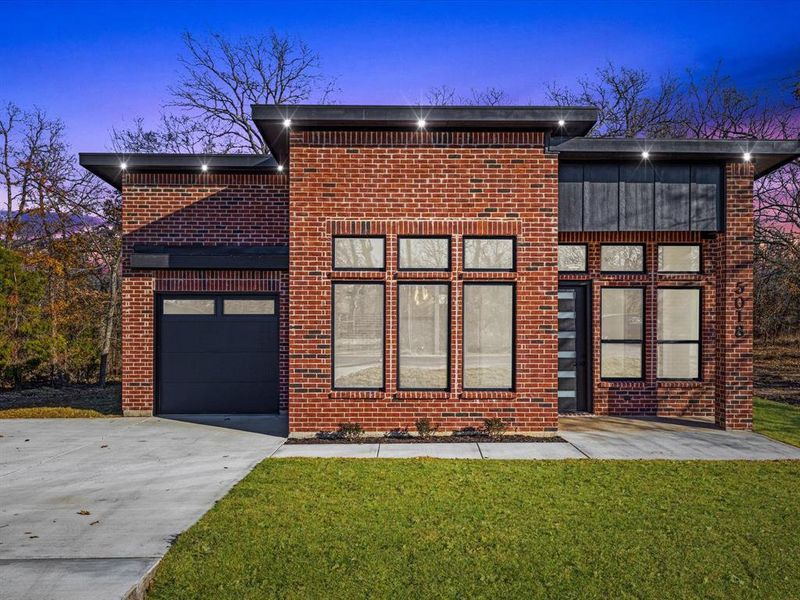 Back of house at dusk with concrete driveway, a yard, an attached garage, and brick siding Back of house at dusk with concrete driveway, a yard, an attached garage, and brick siding