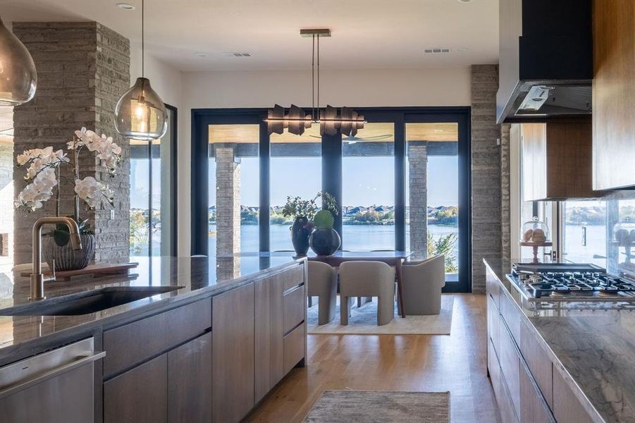 Kitchen with hanging light fixtures, light hardwood / wood-style flooring, a notable chandelier, a water view, and appliances with stainless steel finishes