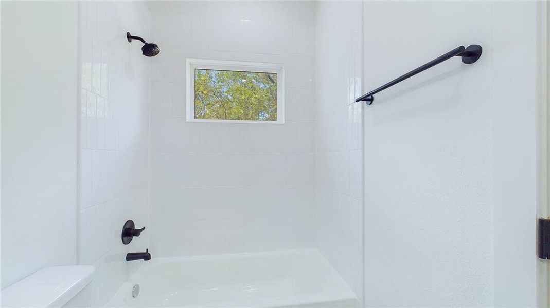 A spacious the tub and shower combo is framed by classic white subway tiles, adn complimented with black hardware, creating a clean and timeless look.